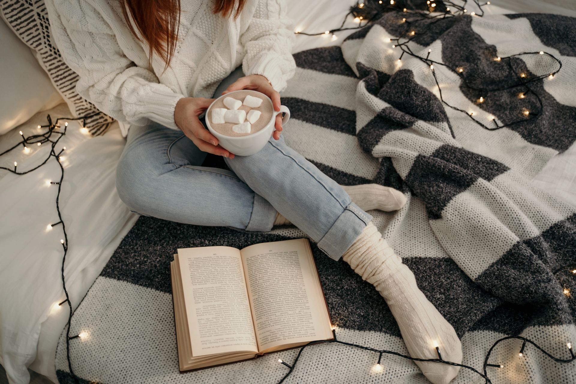 A cozy bed with a warm blanket, fairy lights and a mug of hot chocolate on a winter night