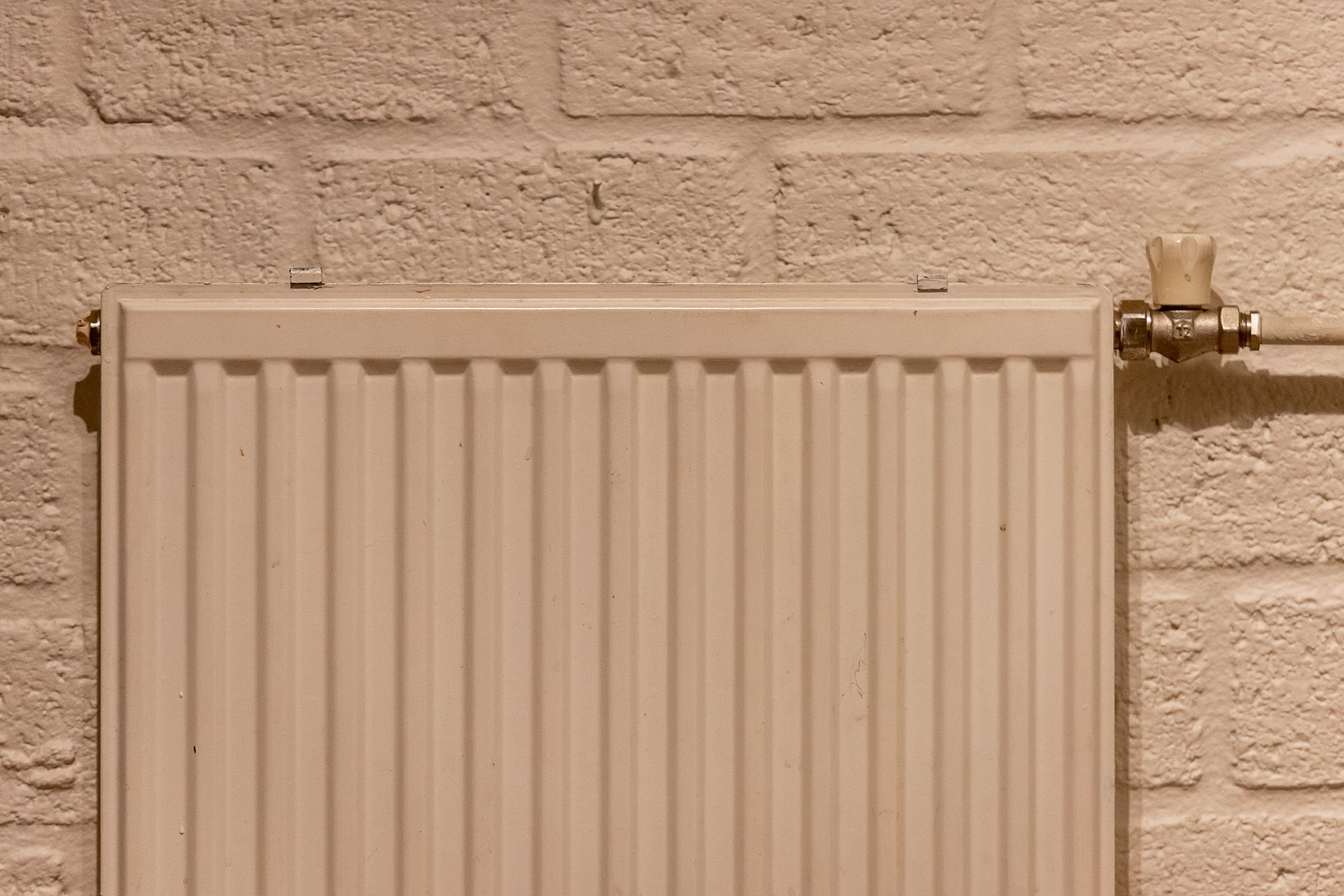 White radiator heater mounted on a textured brick wall