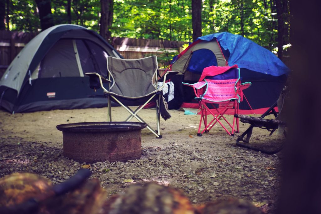 Two folding camping chairs by a fire pit at a wooded campsite