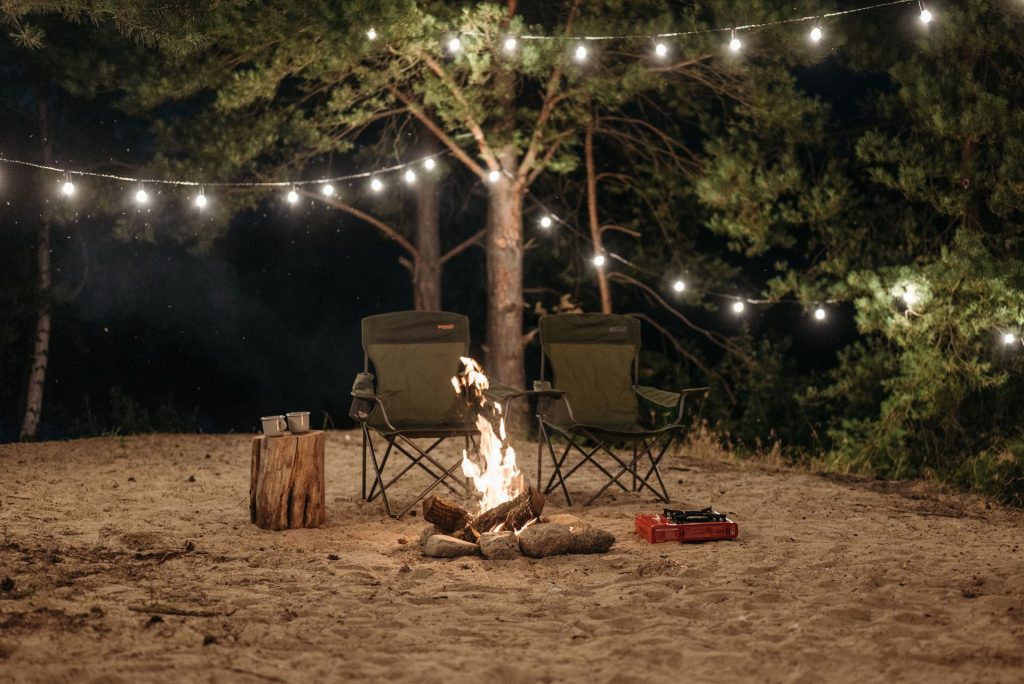 Folding camping chairs around a bonfire with string lights