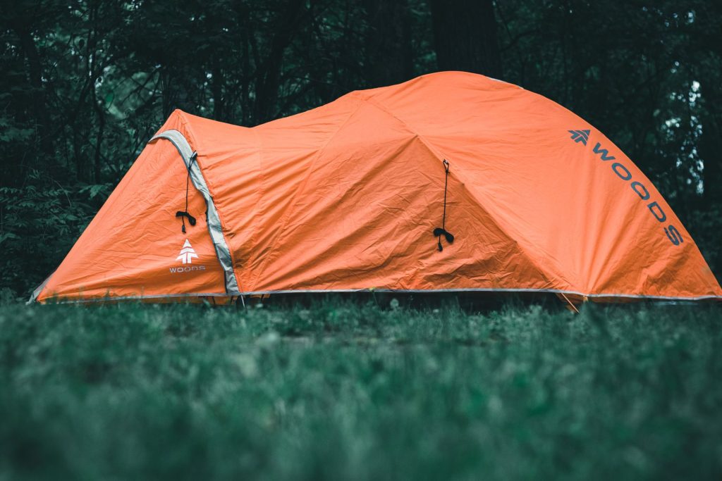 Orange dome tent pitched in a forest clearing